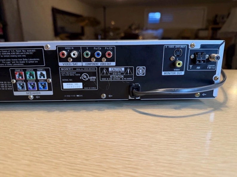 May include: Rear panel of a Sony DVD receiver with various input and output ports, including video, audio, and speaker connections. The panel has labels for Video/Sat, Component Video Out, and Monitor Out. A power cord is connected.