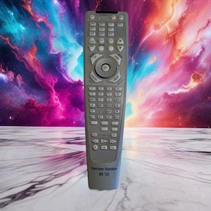 Può includere: Un telecomando argentato Harman Kardon AVR 130 dotato di tastierino numerico, pulsanti di navigazione direzionale e vari tasti funzione per le impostazioni audio e video. Il dispositivo ha una forma rettangolare con una base affusolata.