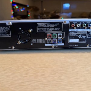 May include: Rear panel of a black and silver Sony DVD receiver. Features various input/output ports, speaker terminals, and a fan. Includes text such as "VIDEO/SAT", "COMPONENT VIDEO OUT", and "SPEAKER".