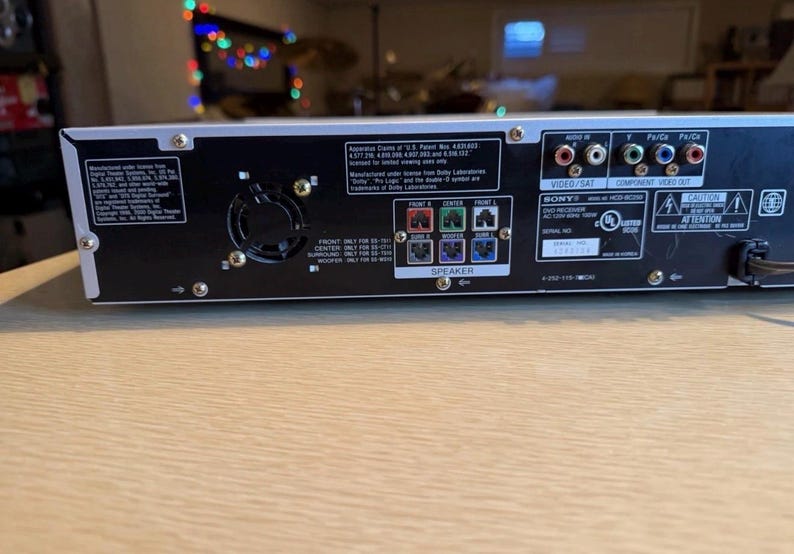May include: Rear panel of a black and silver Sony DVD receiver. Features various input/output ports, speaker terminals, and a fan. Includes text such as "VIDEO/SAT", "COMPONENT VIDEO OUT", and "SPEAKER".
