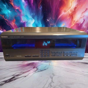 Peut inclure: Un changeur de disques compacts Technics SL-MC7 gris foncé doté d'un affichage numérique central avec du texte bleu, d'un pavé numérique et de divers boutons de commande de lecture. La façade comprend un bouton d'alimentation et une sortie optique.