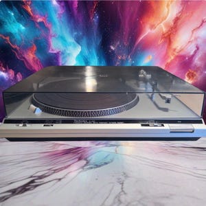 May include: A silver and black Technics SL-B20 Frequency Generator Servo Automatic Turntable System with a clear plastic dust cover. The device features a circular platter, a tonearm, and various control switches on the front panel.