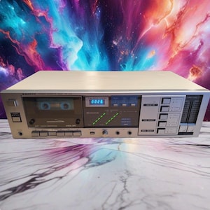 May include: A silver Sanyo stereo cassette deck model RD 540 featuring a front-loading tape compartment, a digital counter displaying 0026, green LED level indicators, multiple control buttons, and two input level sliders on the right side.