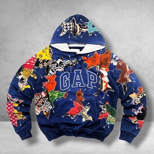 May include: A navy blue hooded sweatshirt featuring the white text GAP across the chest. The garment is decorated with numerous multi-colored fabric patches in various shapes and patterns, all attached with visible white zigzag stitching.