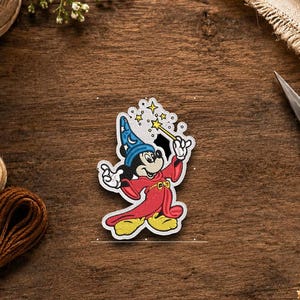 May include: A die-cut sticker featuring a cartoon mouse dressed as a wizard in a blue hat with a crescent moon and stars, wearing a long red robe with yellow accents, and holding a yellow magic wand with sparkling stars above the tip.