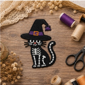 May include: An embroidered iron-on patch featuring a black cat with a white skeleton design, wearing a black witch hat with a purple band and orange buckle, and a small purple spider accent on the tip of the hat, with white whiskers and pink nose.