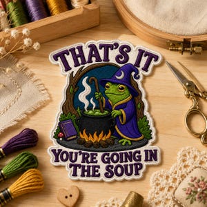 May include: An embroidered patch featuring a green frog wearing a purple wizard hat and robe, stirring a black cauldron over a fire. The text reads THAT'S IT YOU'RE GOING IN THE SOUP in purple letters. The patch has a white border and scalloped edges.