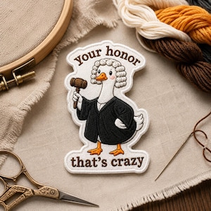 May include: An embroidered patch featuring a white goose wearing a judge's wig and black robe, holding a brown wooden gavel. The text "Your honor" is arched above the goose, and "that's crazy" is written below in brown thread on a white background.