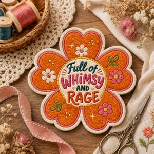 May include: A flower-shaped embroidered patch featuring an orange center with pink borders. The text reads Full of WHIMSY AND RAGE in dark teal and pink. Small white and pink flowers, green leaves, and yellow dots are stitched onto the orange petals.