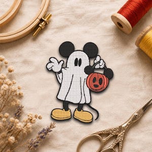 May include: An embroidered iron-on patch featuring a character dressed as a ghost in a white sheet, wearing yellow shoes, and holding an orange jack-o'-lantern bucket with black ears. The design includes black outlines and black mouse ears.