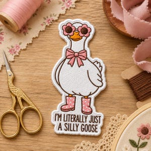 May include: An embroidered patch featuring a white goose wearing pink flower-shaped sunglasses, a pink bow tie, and pink polka-dot rain boots. The patch includes the brown embroidered text "I'M LITERALLY JUST A SILLY GOOSE" at the bottom.