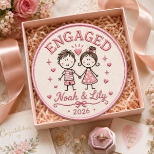 May include: A round embroidered patch featuring a cartoon couple holding hands with the text ENGAGED, Noah & Lily, and 2026. The design includes pink hearts and stars on a cream background with a pink border, presented in a gift box.