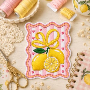 May include: A rectangular embroidered patch with a scalloped edge featuring a pink and white vertical striped background with small pink hearts. The design includes two yellow lemons, one lemon slice, a green leaf, and a yellow ribbon bow.