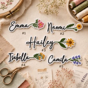May include: Five white fabric patches with black embroidered names Emma, Naomi, Hailey, Isabella, and Camila. Each name is attached to a colorful embroidered wildflower stem. The patches are labeled #1 through #5 in black text.