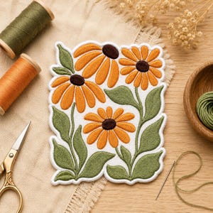 May include: A rectangular embroidered patch featuring three orange flowers with dark brown centers and green leaves on a white background. The patch is surrounded by sewing supplies including two spools of thread, scissors, and a needle.