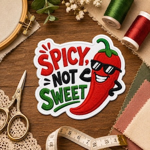 May include: A white embroidered patch featuring a red chili pepper wearing black sunglasses with the text SPICY NOT SWEET in red, black, and green thread. The patch is surrounded by sewing supplies including scissors, thread spools, and a measuring tape.