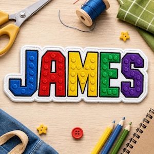 May include: A rectangular embroidered patch featuring the name JAMES in block letters. Each letter has a raised, circular stud texture in a different color: blue for J, red for A, yellow for M, green for E, and purple for S, all outlined in black.