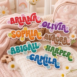 May include: A collection of seven embroidered name patches in various colors, including red, purple, orange, brown, teal, green, and blue. Each patch features a wavy, retro-style font and is decorated with small, multi-colored flower accents.