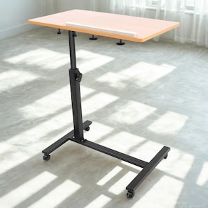 May include: A height-adjustable laptop desk on wheels, featuring a light wood-effect tabletop. The desk has a black metal frame and base with four castors. The tabletop has a small lip and adjustment knobs. The desk is designed for use with a laptop or other devices.