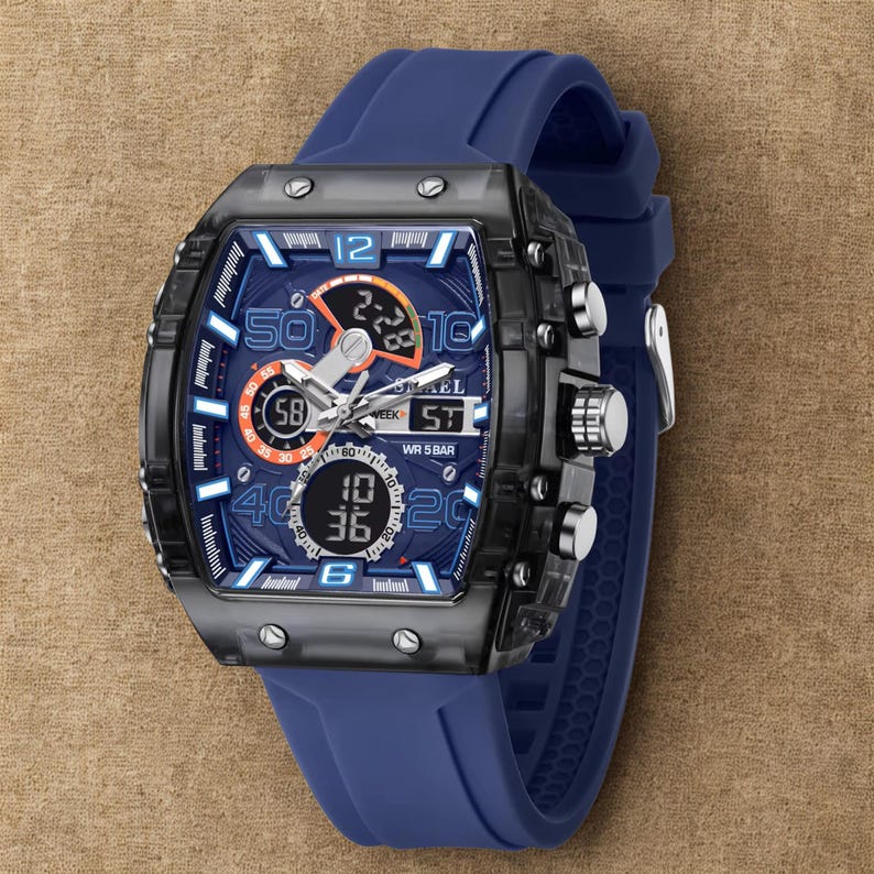 K&ouml;nnte beinhalten: Eine blaue und schwarze Digitalarmbanduhr mit quadratischem Zifferblatt und blauem Silikonarmband. Das Zifferblatt zeigt mehrere digitale Anzeigen und analoge Zeiger. Die Uhr hat silberne Kn&ouml;pfe und eine schwarze L&uuml;nette.