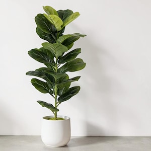 May include: A tall artificial fiddle leaf fig plant with large, dark green, violin-shaped leaves arranged along a central stem. The plant is potted in a smooth, cylindrical white ceramic planter with a flat base and a simple, clean design.
