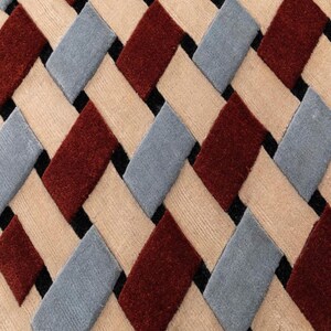 Könnte beinhalten: Ein gewebter Teppich mit einem sich wiederholenden geometrischen Muster aus rechteckigen Segmenten in Dunkelrot, Hellbeige und Schieferblau. Die Segmente sind in einem diagonalen Kreuzmuster angeordnet, mit kleinen schwarzen Lücken.