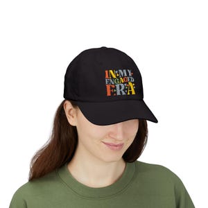 May include: Black baseball cap featuring the embroidered text "IN MY ENGAGED ERA" in various colours. The cap has a curved peak and a classic six-panel design. The hat is worn by a person.