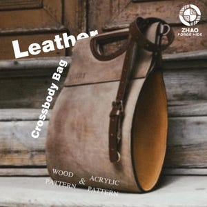 Puede incluir: Un bolso bandolera de cuero color canela estructurado con un perfil lateral redondeado, una correa de cuero marrón oscuro con hebilla de metal y un asa recortada. El bolso presenta el texto Leather, Crossbody Bag, Wood & Acrylic Pattern y Zhao Forge Hide.
