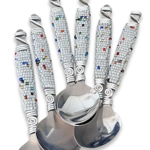 May include: A set of six decorative spoons. Each spoon has a silver handle wrapped with silver wire and decorated with small, colourful beads. The spoon bowls are polished silver, reflecting light.