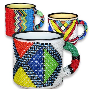 Könnte beinhalten: Drei handgefertigte Tassen mit Perlenmustern. Die Tassen weisen leuchtende Farben wie Rot, Blau, Gelb und Grün auf. Jede Tasse hat ein einzigartiges Muster, wobei auch die Griffe mit Perlen verziert sind. Die Tassen haben eine weiße Innenseite und einen schwarzen Rand.