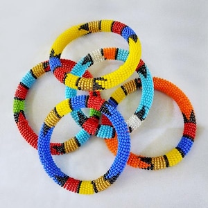 Puede incluir: Una colección de pulseras de cuentas coloridas. Las pulseras son de varios colores, incluyendo amarillo, azul, rojo y naranja, con patrones intrincados. Las pulseras tienen aproximadamente 6,35 cm de diámetro.