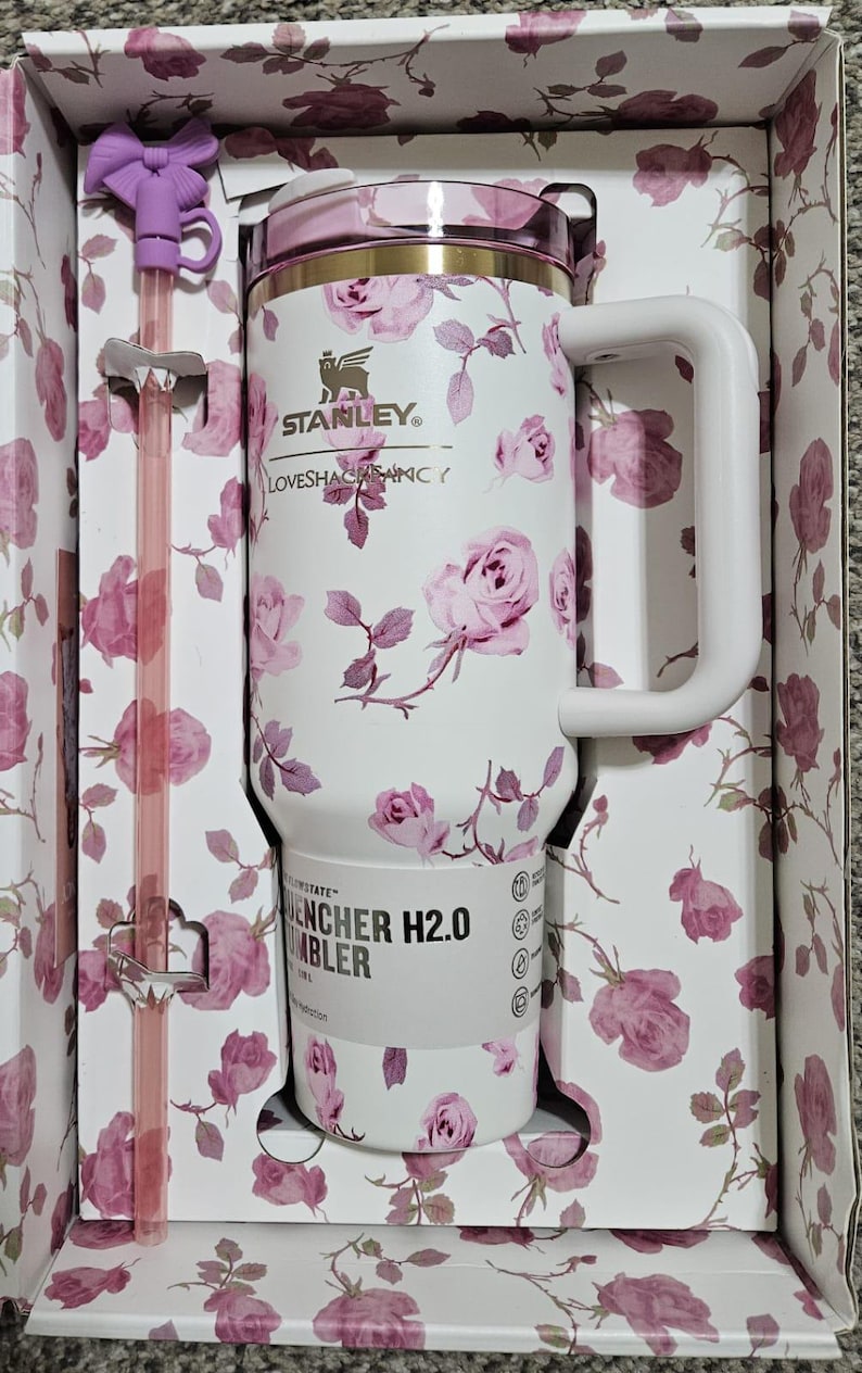 May include: White Stanley Quencher H2.0 tumbler with a pink rose floral pattern, a matching straw, and a bow-shaped straw topper. The tumbler has a handle and is packaged in a floral-printed box.