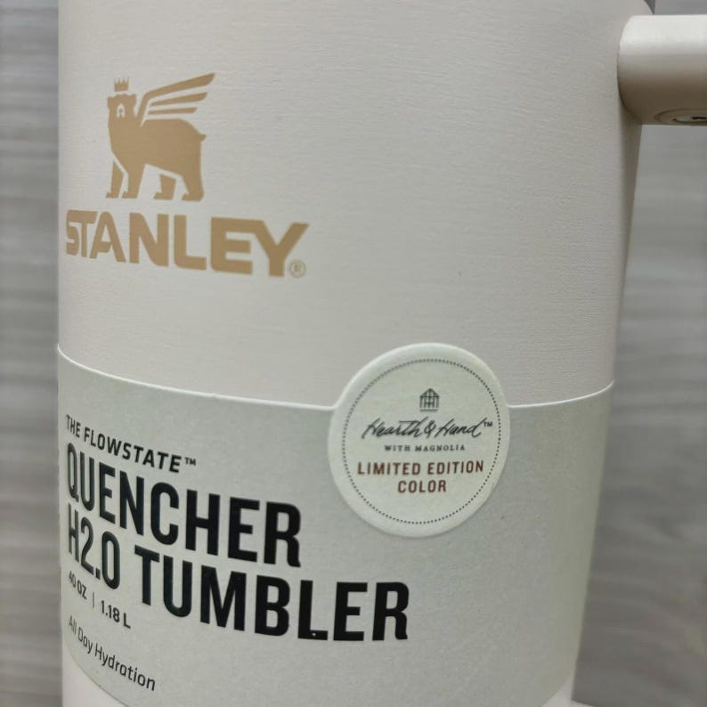 Pu&ograve; includere: Bicchiere Stanley Quencher H2.0 color crema con logo e testo dorati. Il bicchiere ha un manico e un adesivo con la scritta "Hearth & Hand with Magnolia Limited Edition Color". Capacit&agrave; 1,18 L.