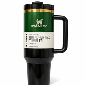 May include: A green and black Stanley Quencher H2.0 Tumbler with a black handle. The tumbler has a black lid and a gold band. The text on the tumbler reads "QUENCHER H2.0 TUMBLER" and "STAY HYDRATED". It holds 40 oz.