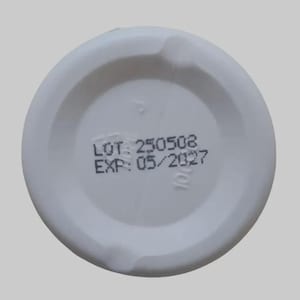 Puede incluir: Tapa de pl&aacute;stico blanco con el texto "LOT: 250508" y "EXP: 05/2027" impreso en negro. La tapa tiene forma circular con un centro rebajado y una superficie ligeramente texturizada.