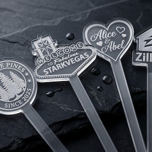 May include: Clear acrylic drink stirrers with various designs. One stirrer says "Under the Pines Since 2025", another says "Welcome to Fabulous Starkvegas", a third says "Alice & Abel", and the last says "Zillow".
