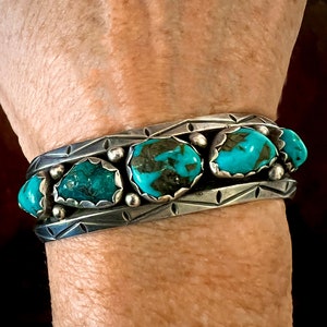 May include: A silver bracelet with a geometric design and five turquoise stones. The stones are set in a silver bezel and are surrounded by silver beads.