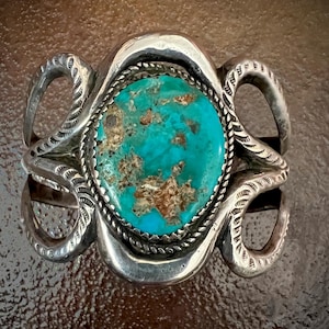 May include: A silver ring with a turquoise stone set in a snake design. The ring is intricately detailed and has a rustic look.