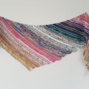 May include: A colorful, hand-knitted shawl with a striped pattern. The shawl features a variety of colors, including pink, yellow, blue, and purple. The edges have a scalloped design. The shawl is displayed against a white background.