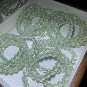 May include: Multiple circular bracelets composed of smooth, translucent pale green beads. Each bracelet features a continuous strand of round, polished stones strung together, displaying a consistent light mint-green hue and a glossy finish.