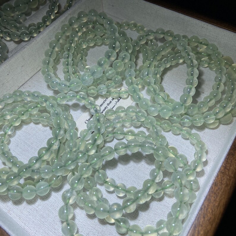 May include: Multiple circular bracelets composed of smooth, translucent pale green beads. Each bracelet features a continuous strand of round, polished stones strung together, displaying a consistent light mint-green hue and a glossy finish.