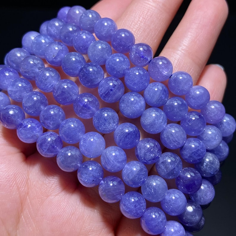 May include: A multi-strand bracelet composed of polished, round, translucent purple beads. The beads exhibit a natural, crystalline texture with varying shades of violet and lavender, arranged in several parallel rows to form a wide, beaded band.
