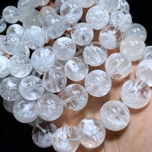 May include: A bracelet composed of multiple spherical, translucent white quartz beads. Each bead features internal cloudy white inclusions and natural fractures, creating a textured, crystalline appearance throughout the circular stone arrangement.