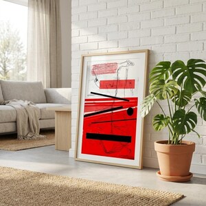 May include: A framed abstract art print featuring a bold red and black design with a minimalist aesthetic. The artwork includes geometric shapes and lines, creating a modern and striking visual. The print is displayed in a light-colored wooden frame.