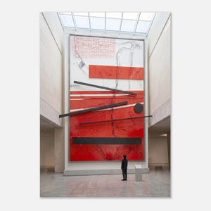 May include: A large abstract artwork with red and black geometric shapes and lines against a white background. The artwork is displayed in a museum setting, with a person standing in front of it, providing scale. The piece features a mix of painted and applied elements.