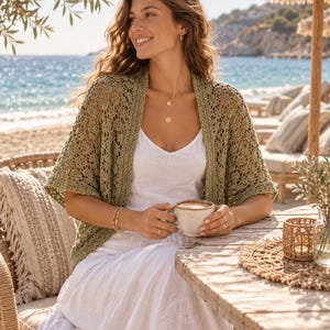 Può includere: Un cardigan aperto color verde oliva caratterizzato da un delicato e intricato motivo a uncinetto con maniche corte, indossato sopra un semplice abito bianco senza maniche. Il capo ha una vestibilità rilassata e un aspetto leggero.