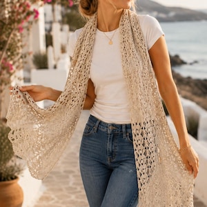May include: A long, beige crochet scarf featuring an intricate openwork pattern with a scalloped edge. The scarf is draped over the shoulders, hanging down the front in two long panels, showcasing the detailed, lightweight, and airy knit construction.
