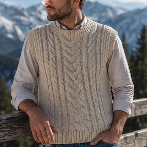May include: A cream-coloured cable knit sweater vest featuring a thick, vertical braided pattern and a ribbed crew neckline. The sleeveless garment is worn over a light-coloured long-sleeved shirt, showcasing a textured, chunky knit construction.
