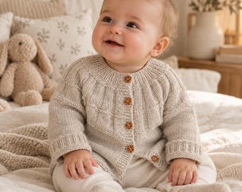 May include: A beige knit cardigan featuring a ribbed yoke, long sleeves with ribbed cuffs, and five small brown floral-shaped buttons down the front. The garment is worn over light-colored pants and matching knit socks.