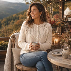 May include: A cream-coloured, long-sleeved knit cardigan featuring a round neckline, a button-down front with three visible buttons, and a delicate lace-like textured pattern across the upper chest and shoulders, paired with blue denim jeans.